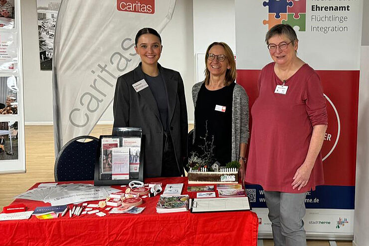 Drei Frauen stehen hinter einem rot-weißen Stand.