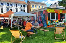 Menschen sitzen auf Bänken vor einem bunt bemalten Container.
